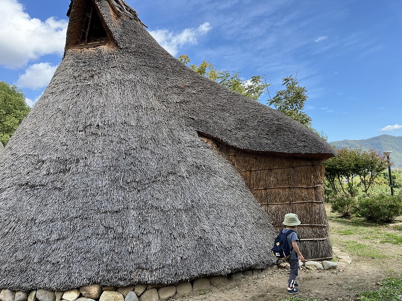 古代体験パークの復元住居の横を歩く子ども